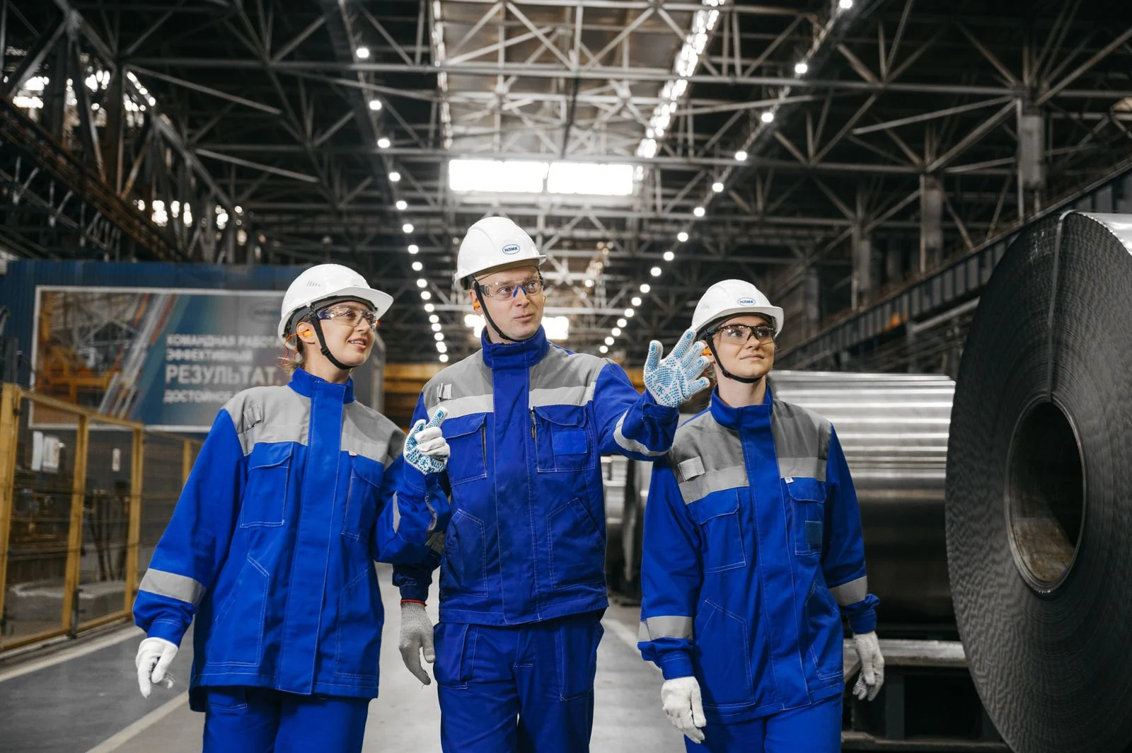 Three industrial workers in protective clothing beside a steel coil